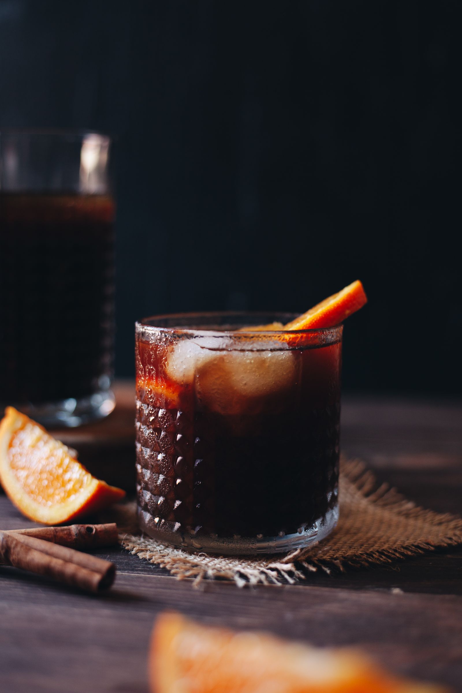 Iced cold brew with orange garnish and citrus on a dark studio surface